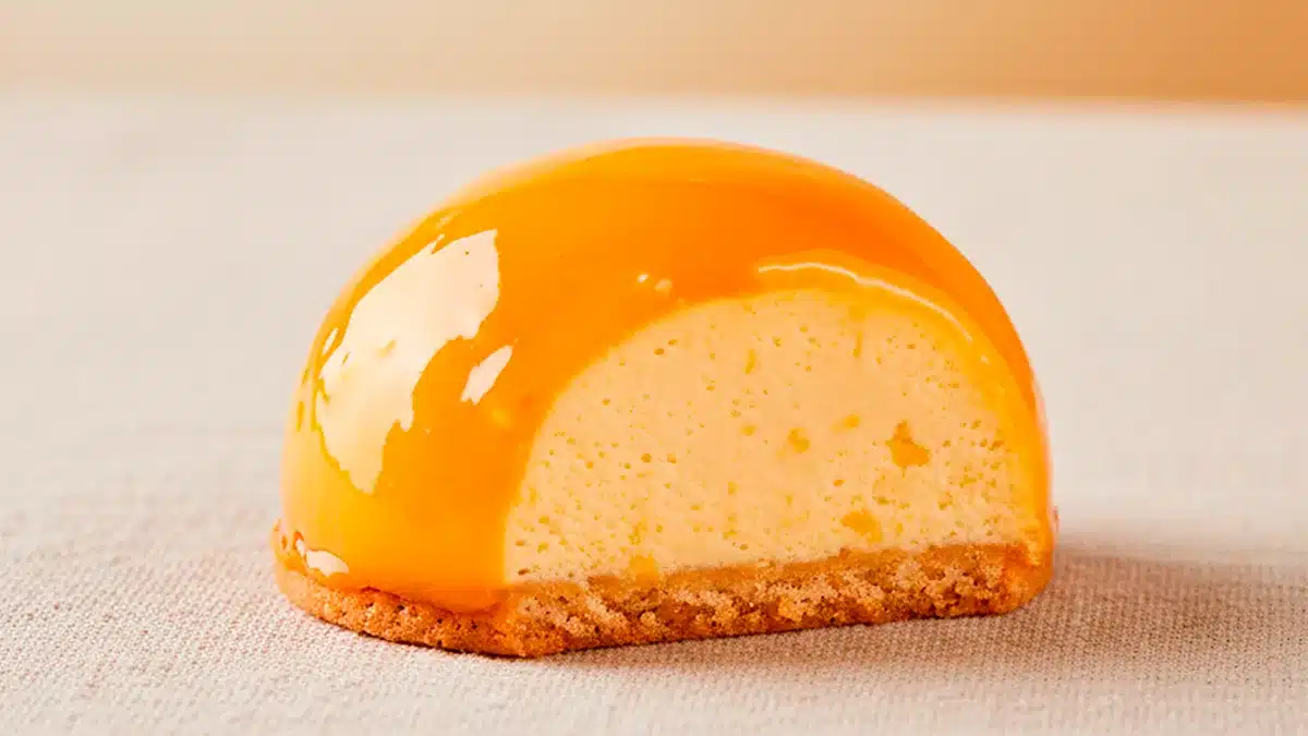 mango_bombon Bombón de mango Montoriens con cobertura dorada y relleno cremoso de chocolate blanco sobre fondo neutro elegante.